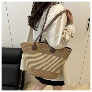 Detail of striped woven tote bag with brown leather straps shown on a shoulder