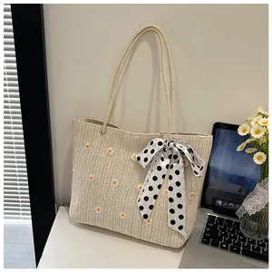 Detail of woven straw tote bag featuring daisy embroidery and polka dot silk bow decoration