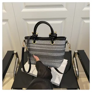 Detail of grey striped woven tote bag featuring knotted black leather handles and hardware