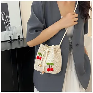 Detail of white woven bucket bag featuring 3D red cherry accents and drawstring strap