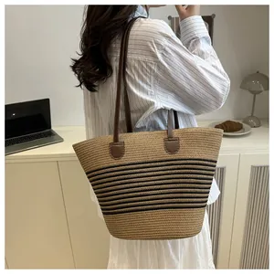 Detail of handwoven straw tote bag with black stripes and brown leather shoulder straps
