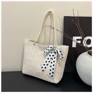 Detailed close-up of straw tote bag with daisy embroidery and polka dot ribbon bow