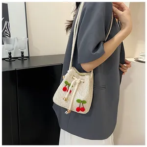 Detail of straw bucket bag with cherry charms and drawstring closure on a shoulder strap