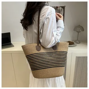 Detail of a large striped straw tote bag with brown leather handles worn by a model