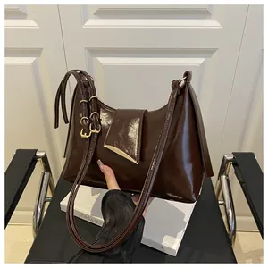 Detail of dark brown glossy leather shoulder bag with gold triangular metal buckle