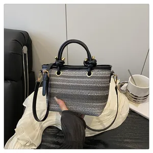 Detail of grey striped woven handbag with black leather handles and gold-toned hardware