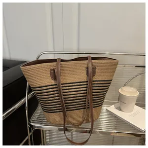 Macro view of woven straw tote bag featuring black stripes and brown leather straps