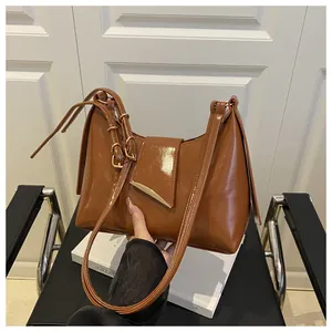 Detail of a brown glossy leather saddle bag with gold metal clasp and adjustable strap