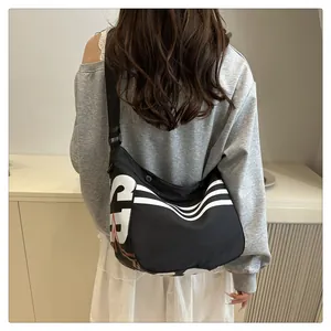 Détail du grand sac à bandoulière noir montrant des lettres blanches et des trois rayures