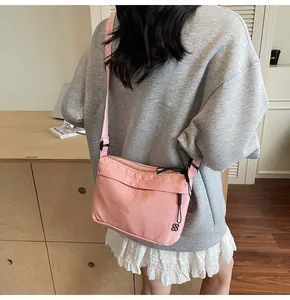 Pink nylon crossbody bag with adjustable shoulder strap shown in a lifestyle casual setting
