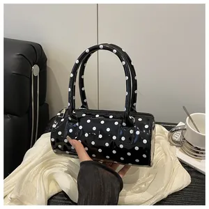 Detail of a black mini cylindrical handbag with white polka dots and glossy finish