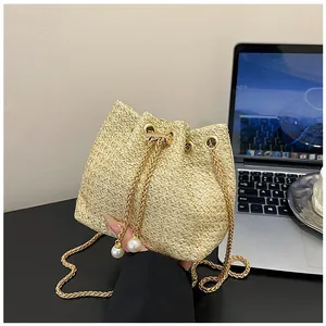 Close-up of beige woven bucket bag with gold chain strap and elegant pearl drawstring charms