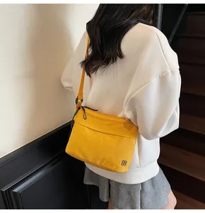 Close-up of bright yellow nylon crossbody bag featuring double zippers and a metal logo