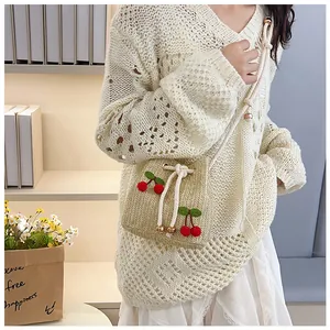 Detail of straw bucket bag with red cherry knit patches and white drawstring closure