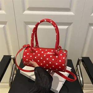 Red patent leather cylinder handbag with white polka dots and adjustable shoulder strap