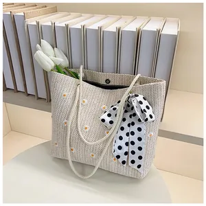 Detail of woven tote bag with daisy embroidery, rope handles and a polka dot bow
