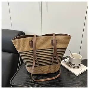 Detail of striped woven straw tote bag with brown faux leather handles and white stitching