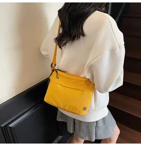 Detail of yellow nylon crossbody bag with silver clover logo and zipper compartments