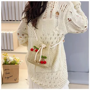 Detail of straw bucket bag featuring 3D red cherry accents and white drawstring closure