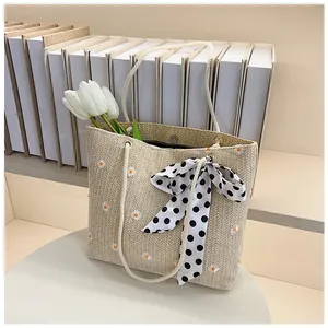 Close-up of woven straw tote bag with daisy embroidery and polka dot silk scarf detail