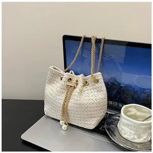 Detail of woven straw bucket bag featuring gold chain and elegant large pearl charms