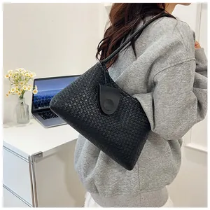 Detail of a black woven shoulder bag with round clasp in a minimalist office setting