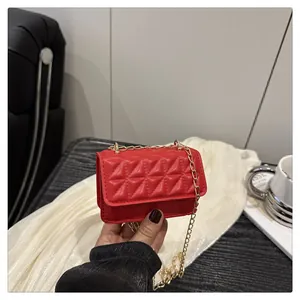 Detail shot of a red mini quilted crossbody bag with a gold chain strap held by hand