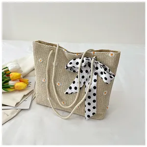 Detail view of woven straw tote bag with daisy embroidery and polka dot ribbon bow