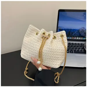 Close-up of woven straw bucket bag with drawstring closure and pearl charm details