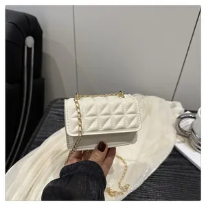 Close-up of white quilted mini crossbody bag with gold chain strap held by hand