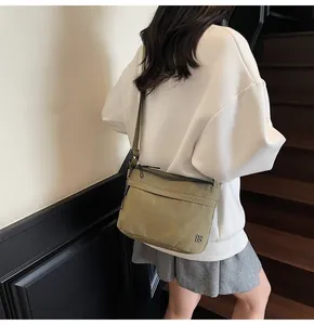 Detail of olive green nylon crossbody bag featuring a silver clover logo and zipper pockets