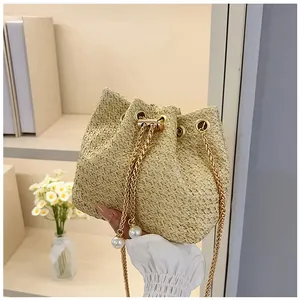 Detail of woven straw bucket bag featuring gold chain strap and large pearl drawstring accents
