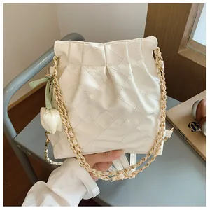 Close-up of quilted white bucket bag with gold chain strap and floral charm detail