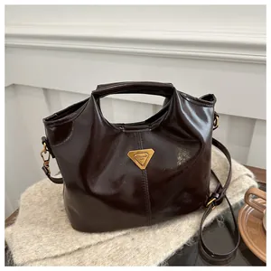 Detailed view of dark brown patent leather handbag with gold triangular metal logo