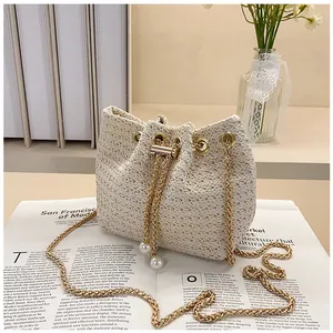 Detailed view of cream woven bucket bag with gold chain and large pearl drawstring accents
