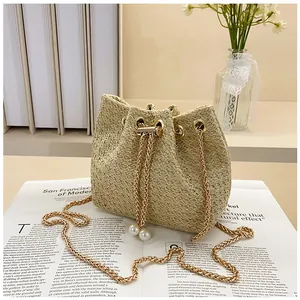 Detail view of cream woven bucket bag with pearl drawstring tassels and gold chain strap