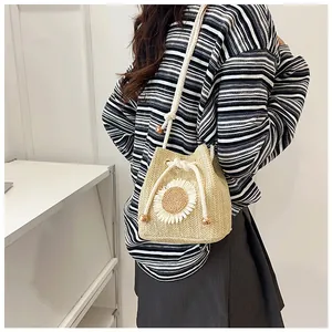 Detail of a beige woven straw bucket bag featuring a white sunflower appliqué and rope strap