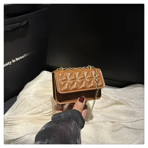 Detail of camel quilted bag with triangle pattern and gold chain strap held by hand