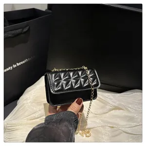 Close-up of black quilted mini square bag with golden chain strap and glossy finish
