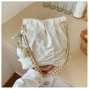 Close-up of beige quilted leather handbag with gold chain strap and floral charm detail