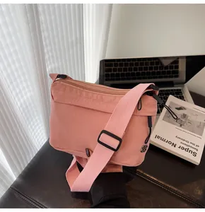 Pink nylon crossbody bag with adjustable wide strap and floral logo in minimalist office setting