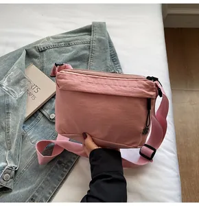 Detailed view of pink nylon crossbody bag with floral zipper pull on blue denim