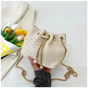 Detail of woven straw bucket bag featuring gold chain strap and large pearl drawstring charms