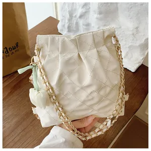 Close-up of quilted cream bucket bag with gold chain and white tulip charm detail