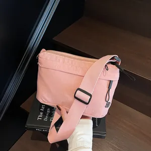 Pink nylon crossbody bag with wide adjustable strap and floral charm on wooden steps