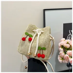 Detail of straw bucket bag with red cherry embroidery and white drawstring closure