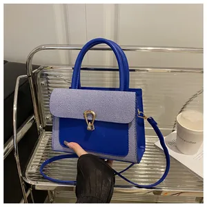 Detail of blue leather and striped fabric handbag with gold U-shaped metal lock