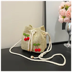 Detail of straw bucket bag featuring 3D cherry accents and a white drawstring closure