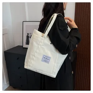 Detalle de bolso tote de nailon blanco con bolsillo frontal y etiqueta de tela en contraste