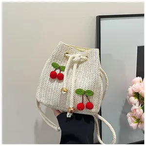 Detail of straw woven bucket bag with 3D red cherry accents and a drawstring closure